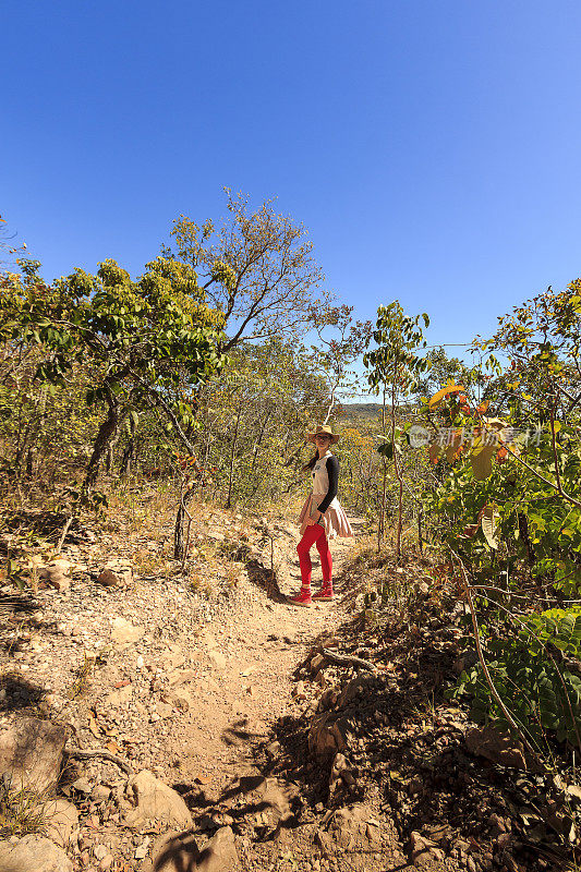 这是一个晴朗的晴天，10岁的女孩站在Chapada dos Veadeiros的一条小路上看着相机